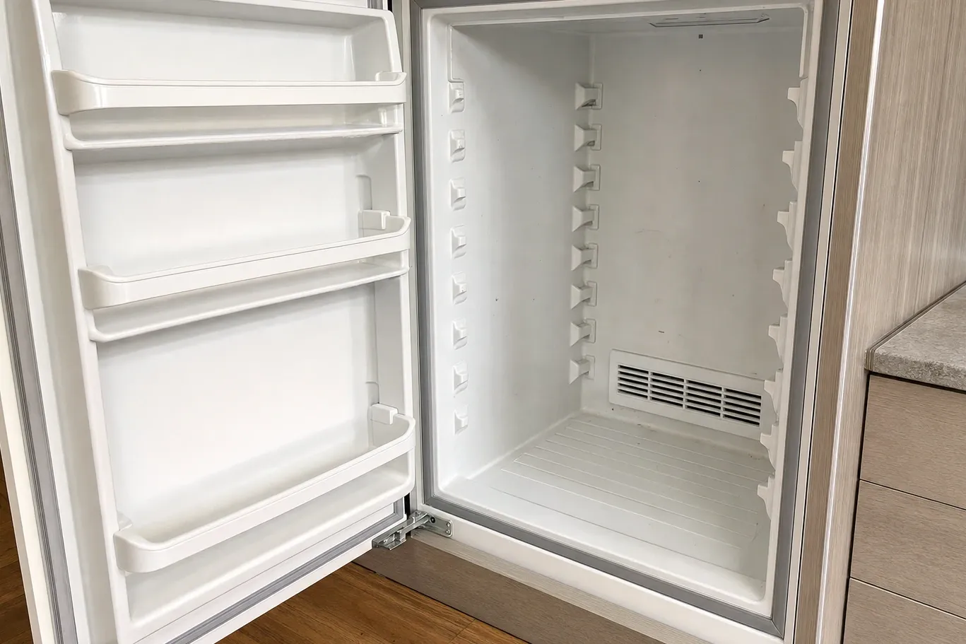 Built-in refrigerator column standing empty, door bins and shelf supports bare, vent grille low at the back
